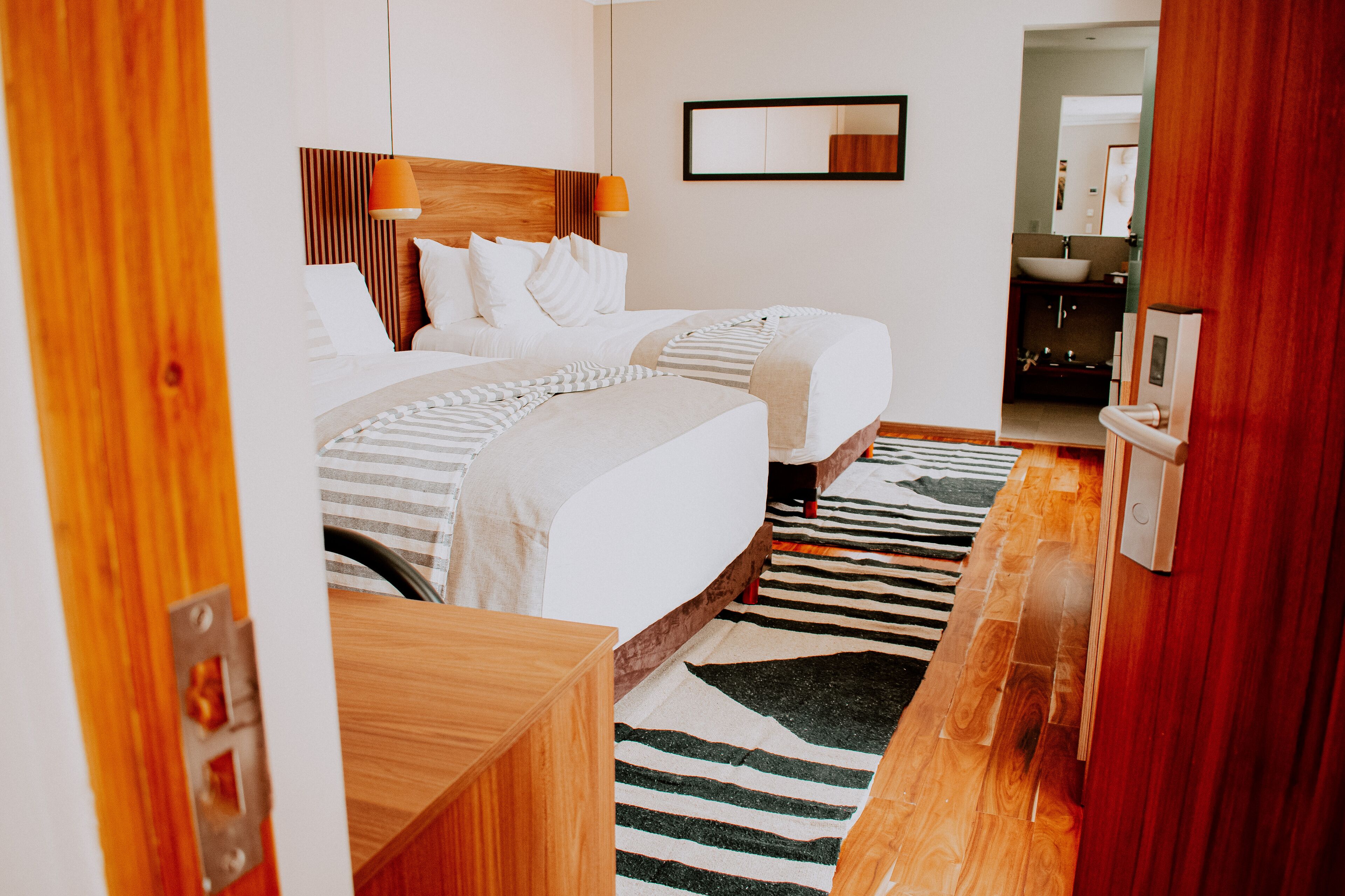 Quarto de hotel com uma cama grande, mesa de cabeceira, espelho e banheiro visível por uma porta aberta.