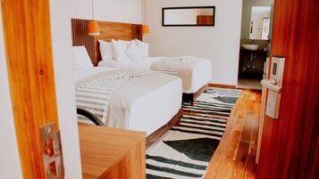 Quarto de hotel com uma cama grande, mesa de cabeceira, espelho e banheiro visível por uma porta aberta.