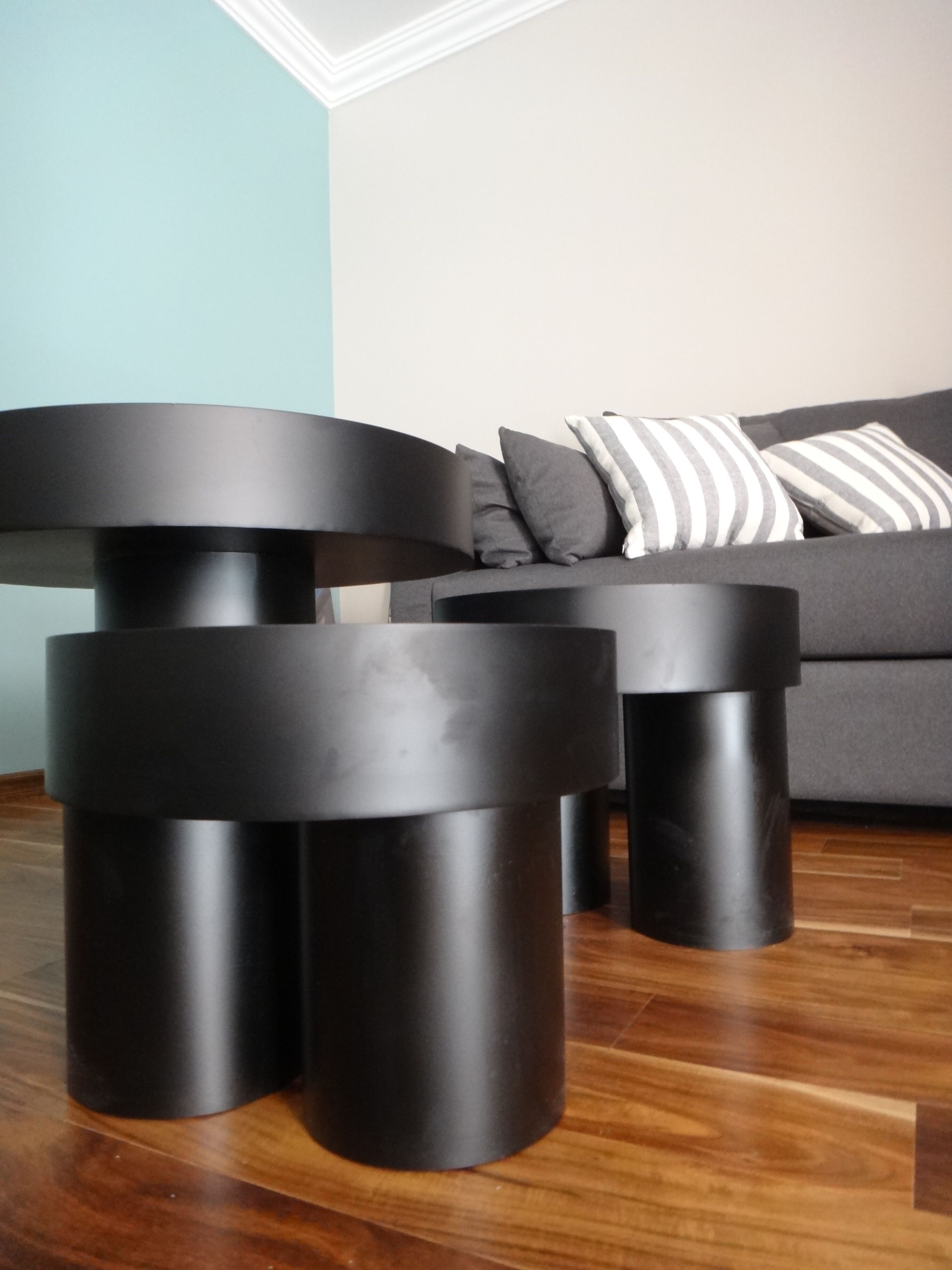 A modern living room with a grey sofa and black cylindrical side tables.