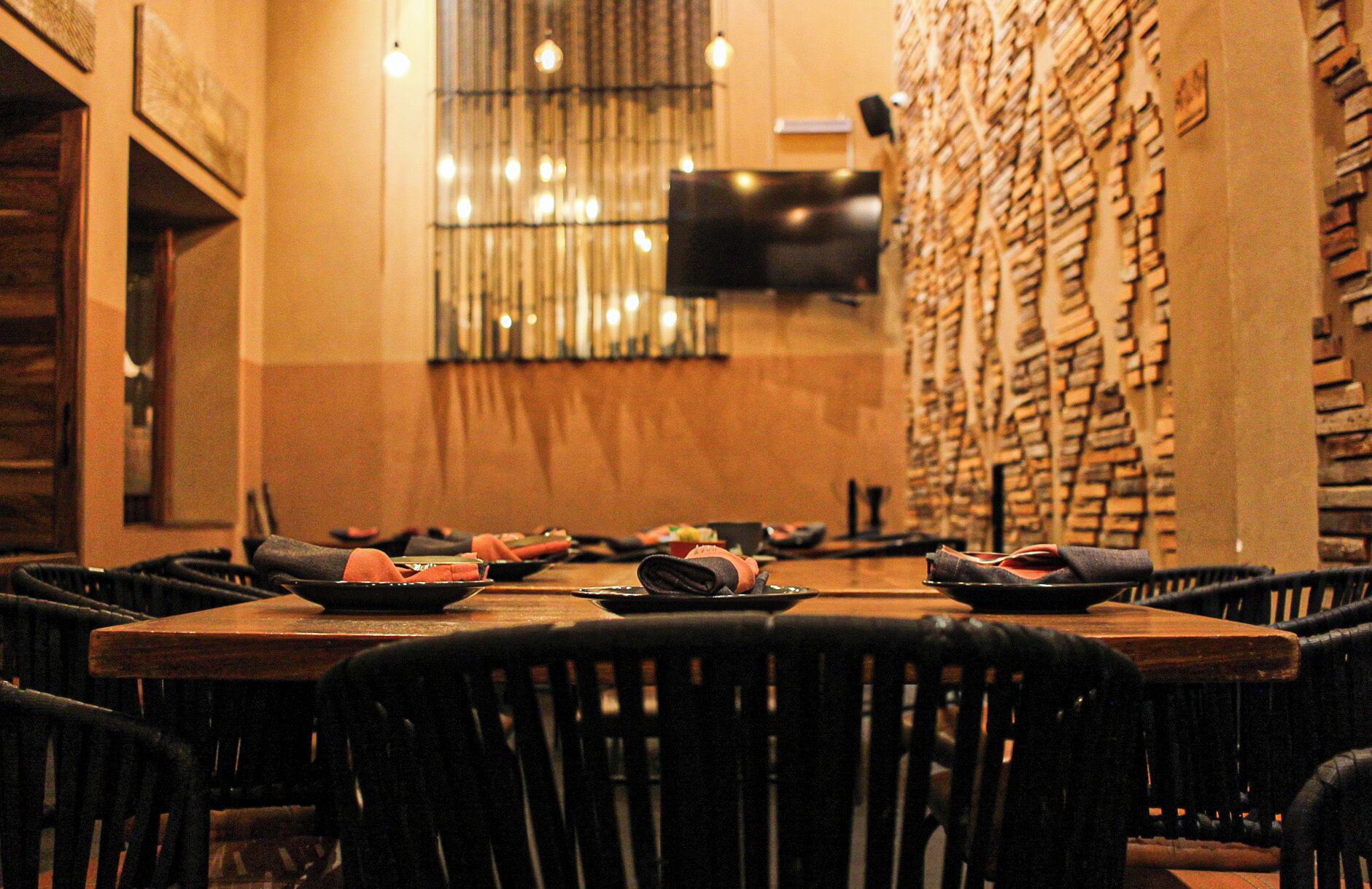 A restaurant with a long table set for multiple guests, chairs around the table, and a wall with a unique brick pattern.