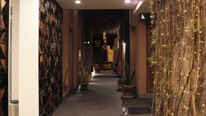 Un couloir avec une bibliothèque sur le côté gauche, des plantes en pot le long du côté droit et un panneau indiquant les toilettes.