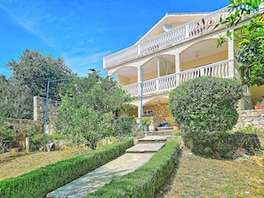 A two-story building with a balcony, stone walls, and a stone pathway leading to the entrance.