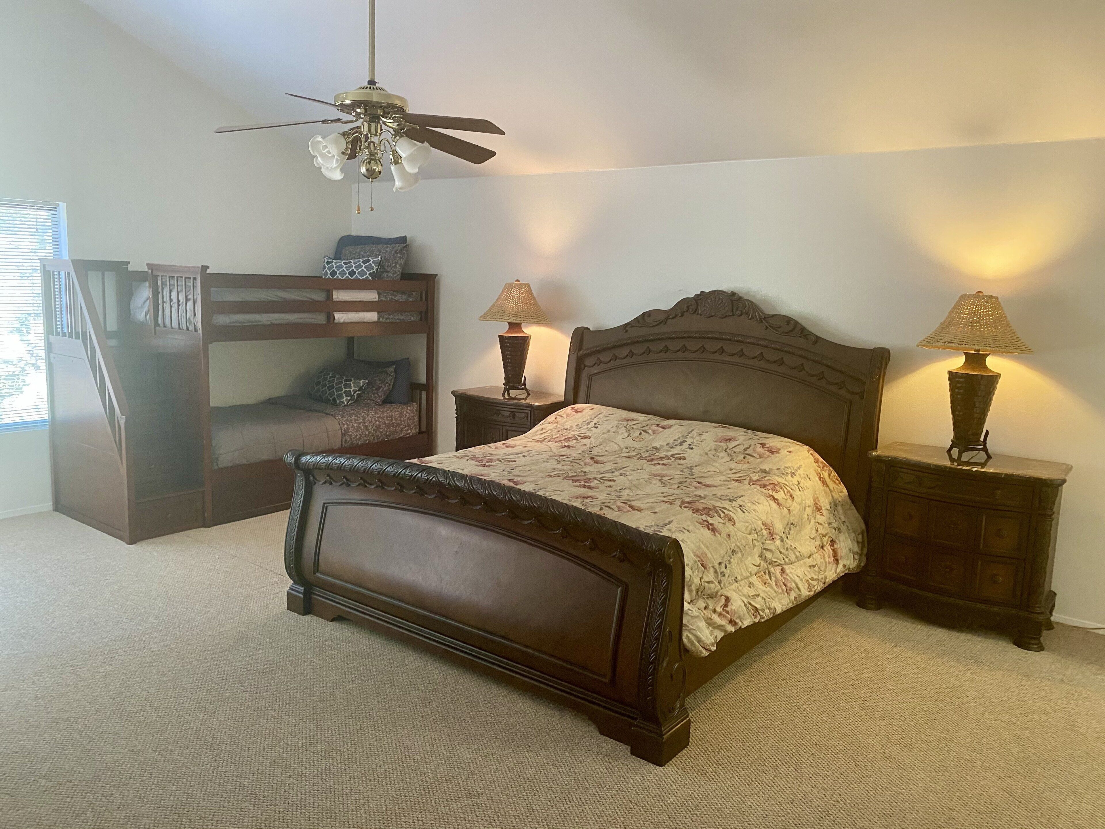 Ein Schlafzimmer mit einem Bett, einem Nachttisch, einer Lampe, einem Deckenventilator und einem Stockbett.