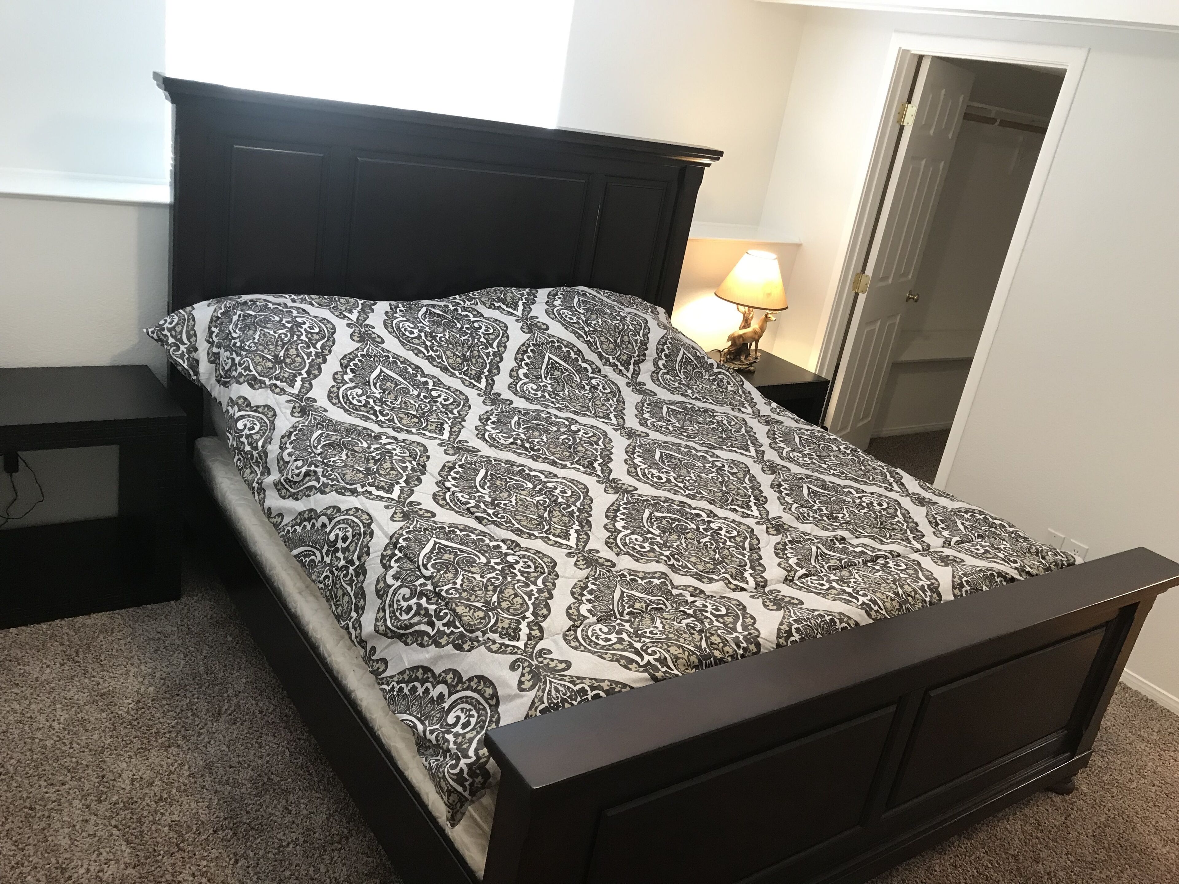 A bed with a patterned bedspread, a dark headboard, and a bedside table with a lamp.