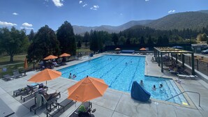 A swimming pool with lounge chairs and umbrellas, surrounded by trees and mountains in the background. - Quail Run 4,000 Sq.Ft Largest and Most Beautiful Cabin On The Mountain (Pine Mountain Club)