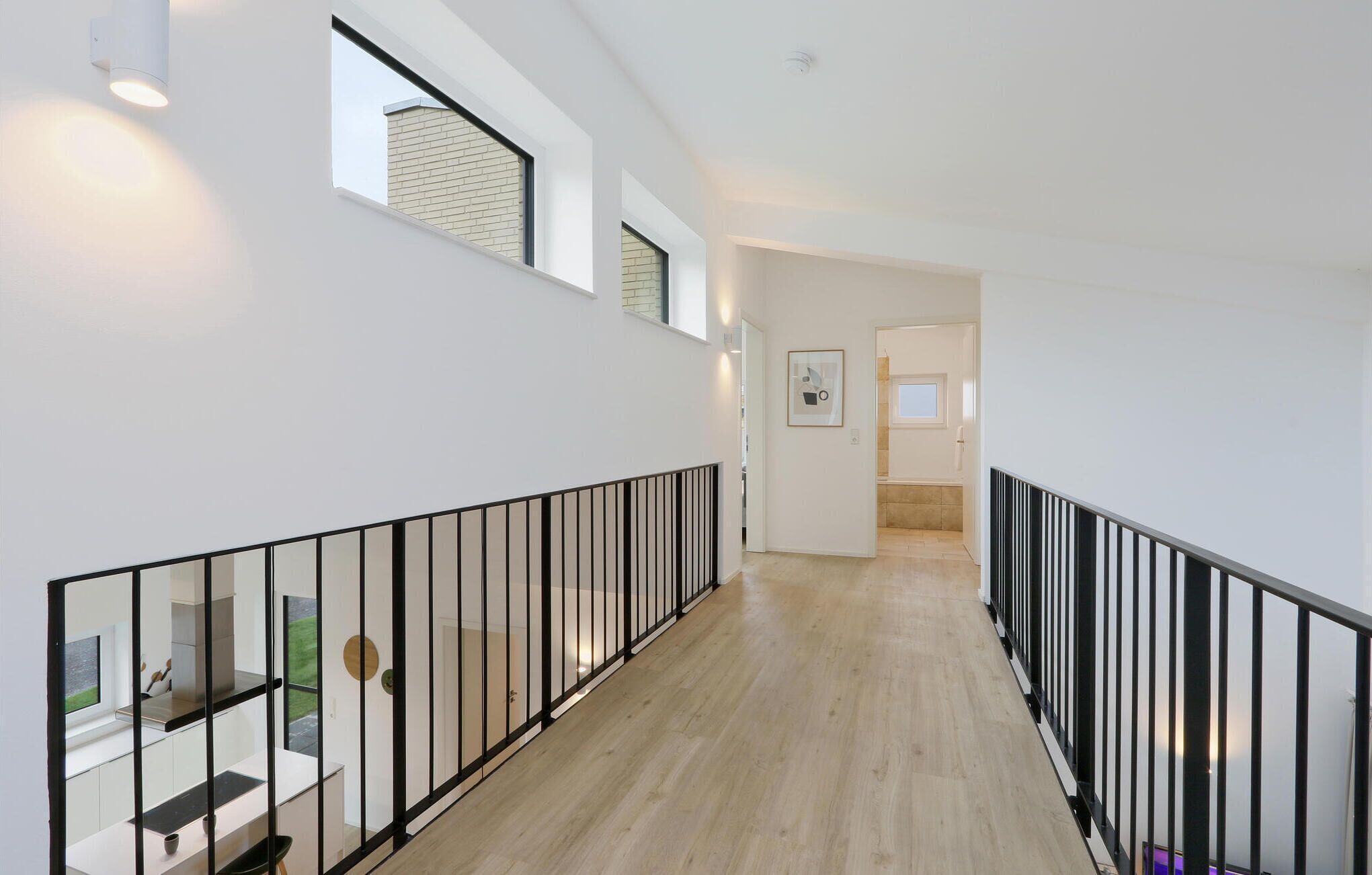 A modern interior with a wooden floor, white walls, and black railings.