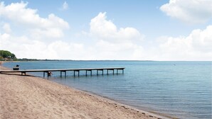 A beach with a wooden pier extending into calm waters, a sandy shore, and a clear sky. - 4 bedroom cozy home in Haderslev (Haderslev)