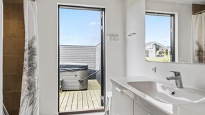 A modern bathroom with a large sink, a mirror, and a sliding door leading to an outdoor area with a wooden deck and a hot tub. - 4 bedroom cozy home in Haderslev (Haderslev)