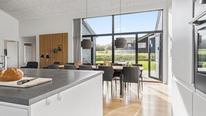 A modern kitchen with a large island, dining area with chairs, and a view of the outdoors. - 4 bedroom cozy home in Haderslev (Haderslev)
