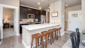 Una cucina moderna con mobili in legno scuro, un'isola bianca con sgabelli da bar, elettrodomestici in acciaio inossidabile e illuminazione a sospensione.