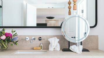 A modern bathroom with a large mirror, a round mirror, a sink, a towel rack, and a small stool.