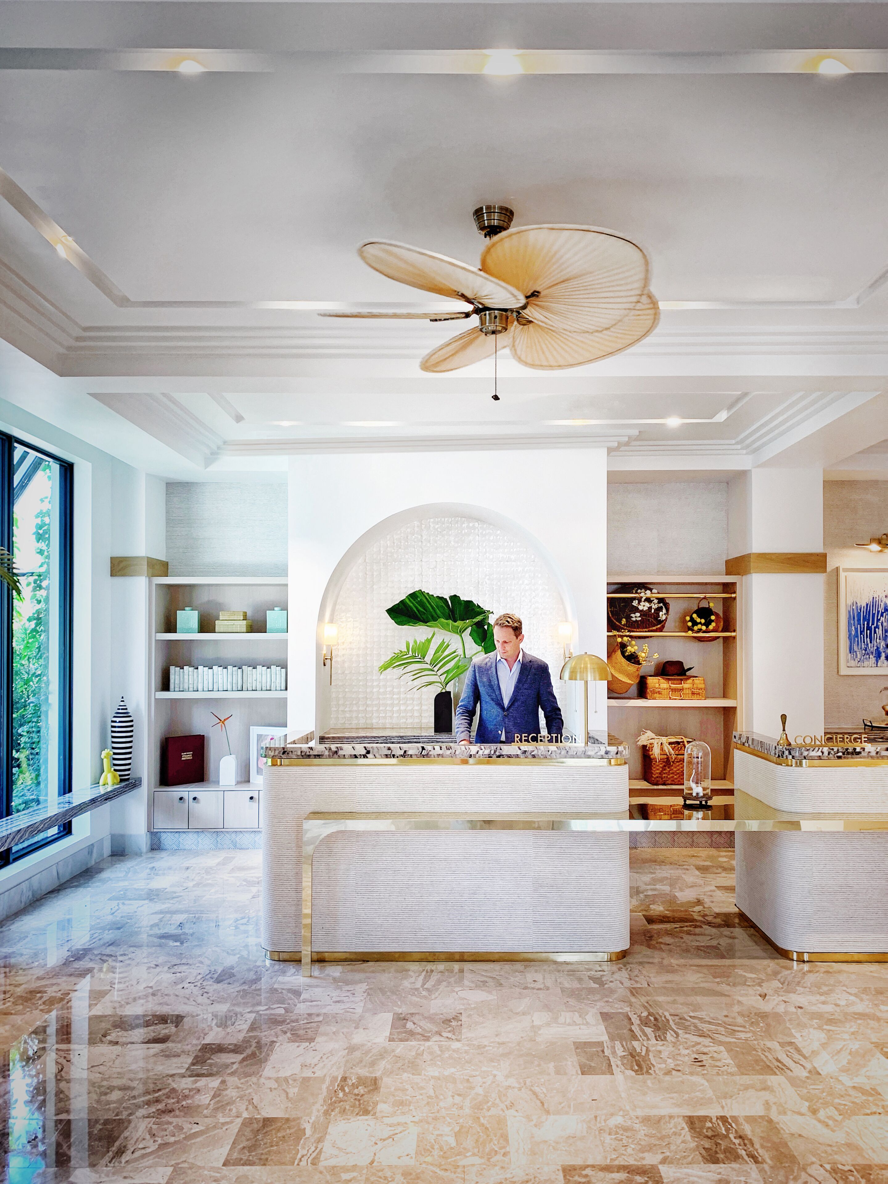 A reception area with a ceiling fan, marble flooring, and a large window with a view of greenery.
