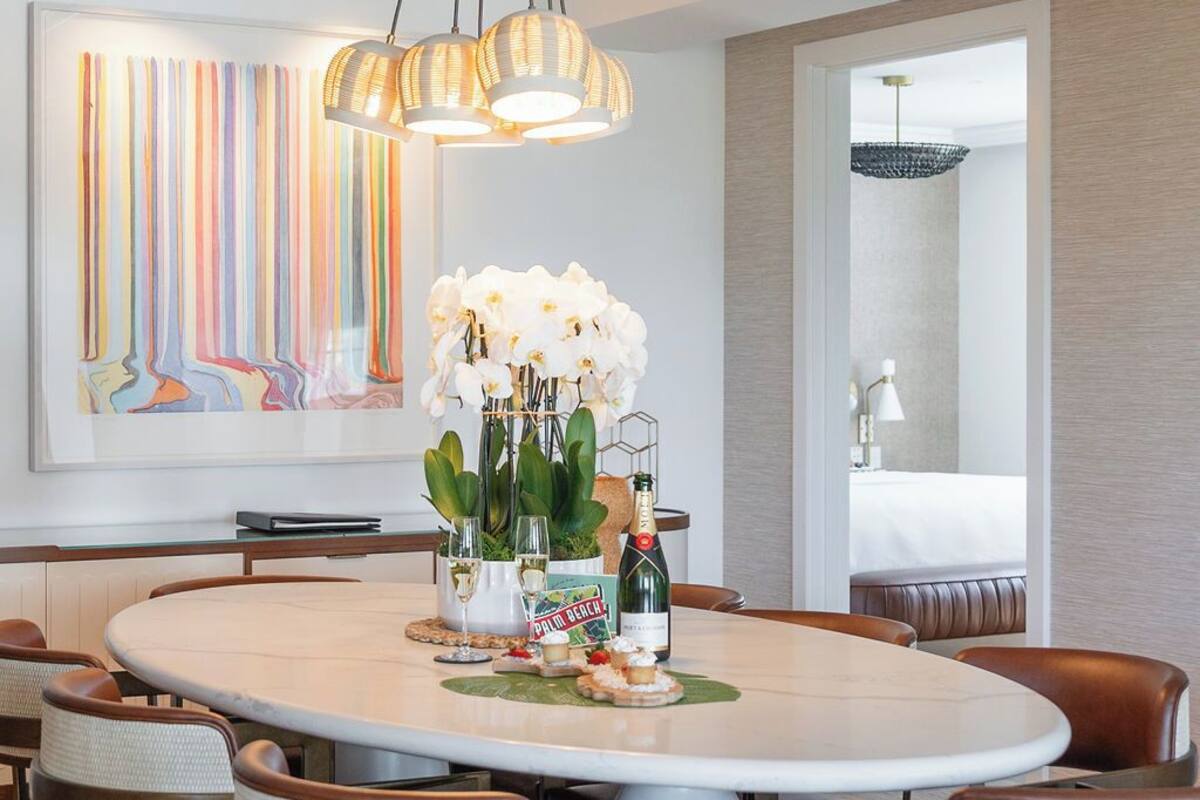 A dining area with a round table, brown leather chairs, a vase of white orchids, and a bottle of champagne.