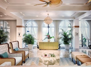 A spacious living room with a high ceiling, large windows, and a central yellow cabinet.