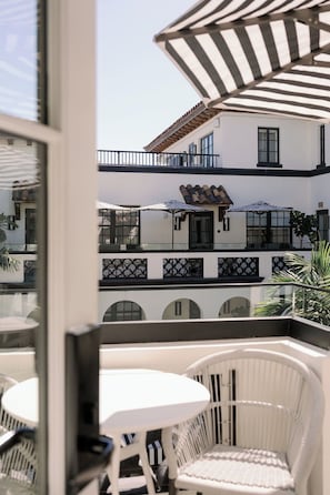 A balcony with white wicker chairs and striped umbrellas, overlooking a building with multiple balconies and a tiled roof.