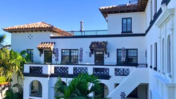 Un edificio de varios pisos con paredes blancas, barandales negros y techo de tejas.