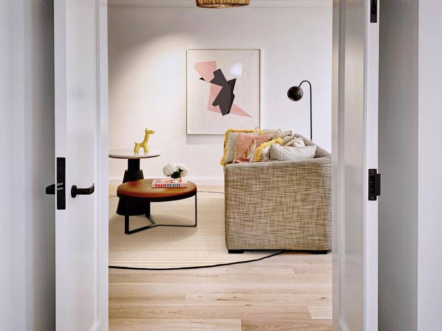 Un couloir mène à un salon où se trouvent un canapé, une table basse, une lampe et un luminaire suspendu.