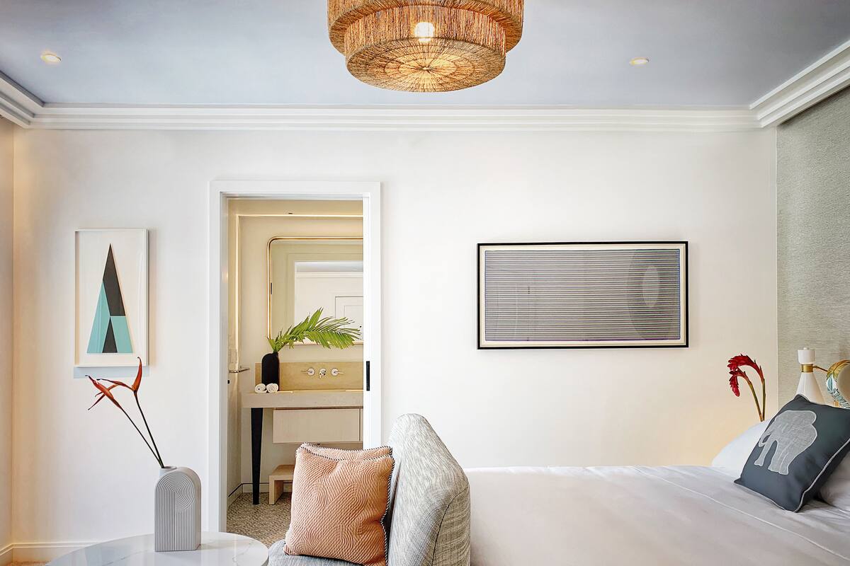 A modern hotel room with a sofa, a round table, a bed, and a bathroom with a mirror and sink.