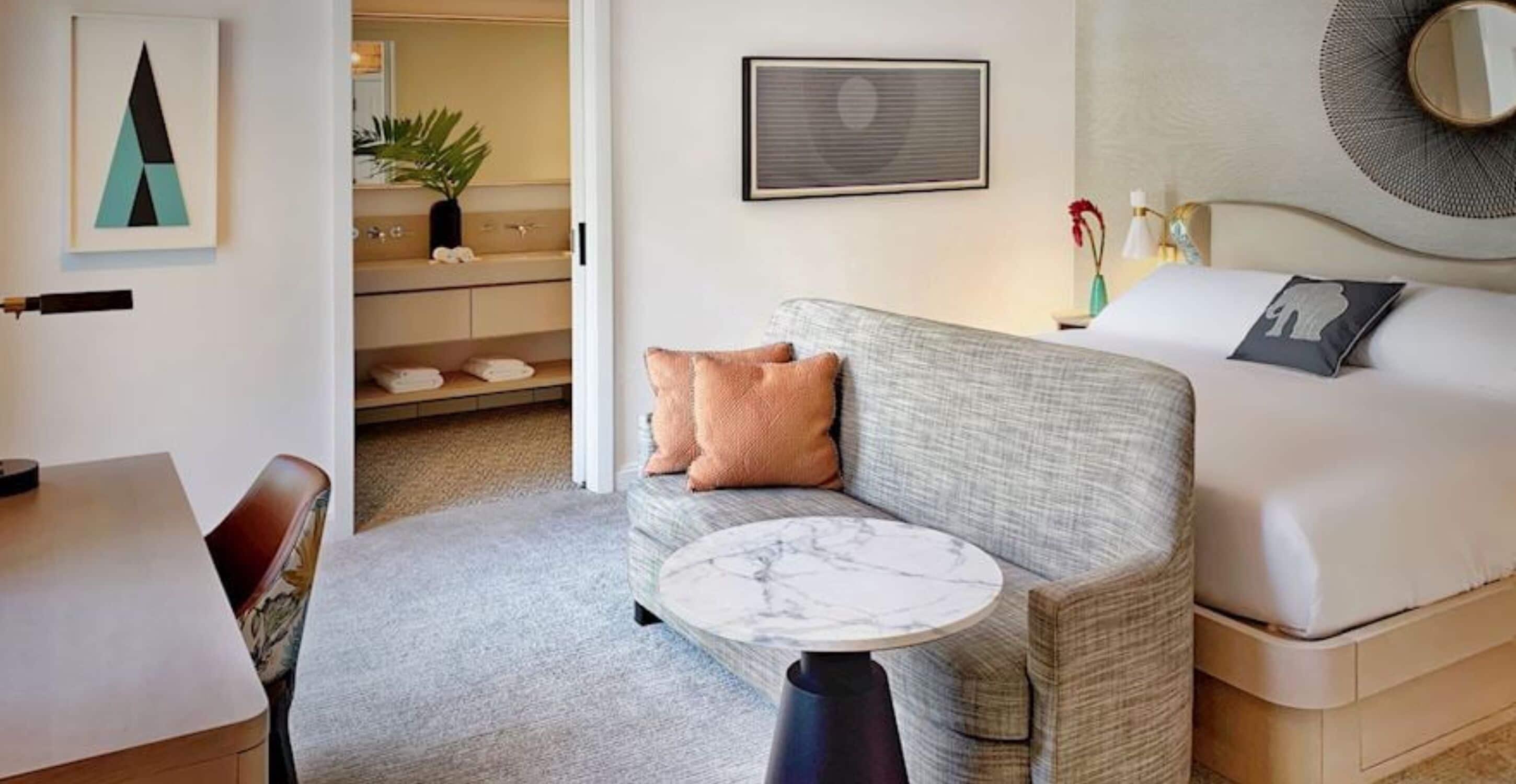 Una habitación de hotel con sofá, una mesita redonda, cama, mesita de noche y espejo.