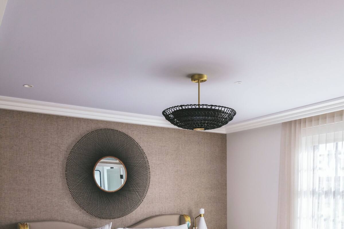 A bedroom with a large bed, a round mirror, a bedside table, a lamp, and a window with curtains.