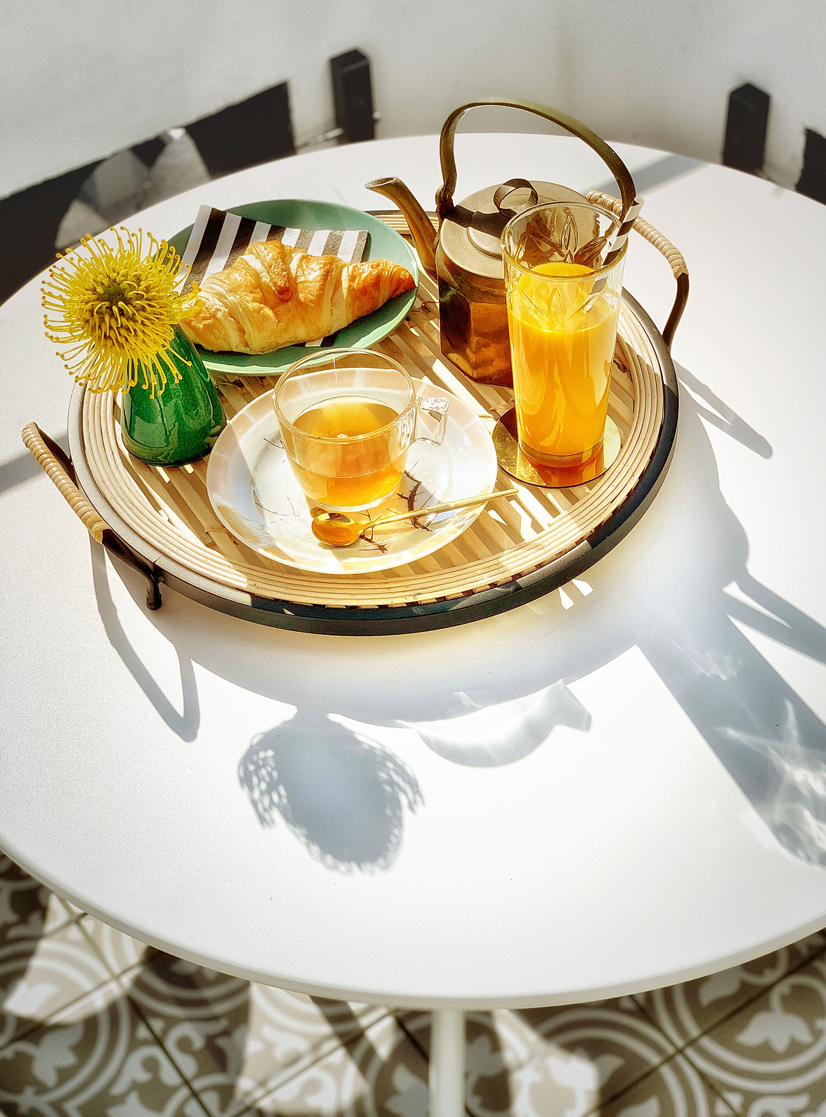 Ein runder Tisch mit einer Ablage, auf der ein Teekessel, ein Glas Orangensaft, eine Tasse Tee und ein Gebäckstück stehen.