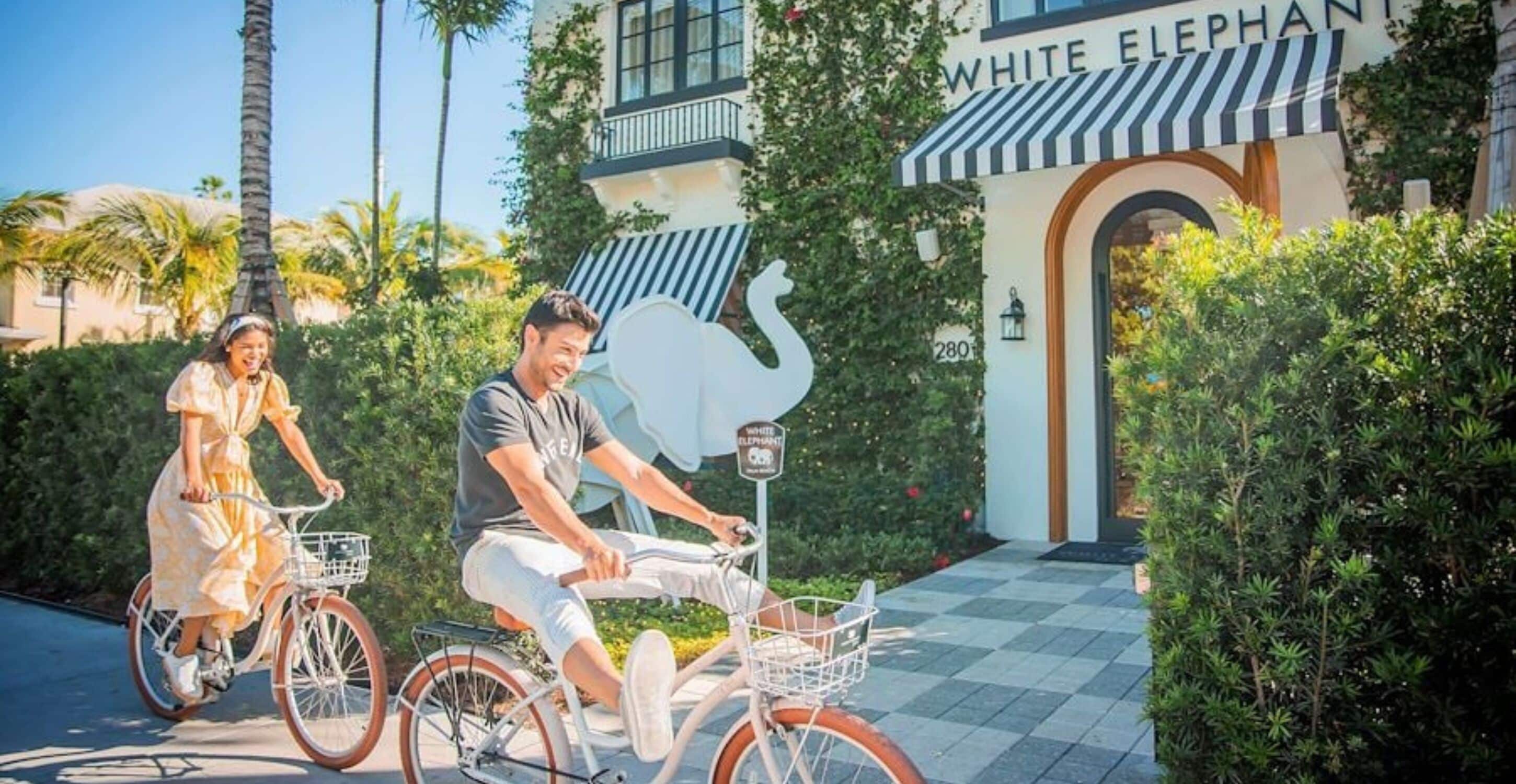 A man and a woman on bicycles in front of a building with a swan sign and the name "WHITE ELEPHANT".