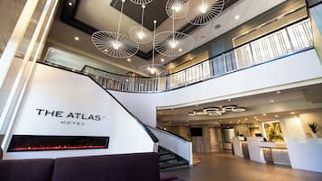 Un vestíbulo de hotel con diseño moderno, que incluye una escalera, mostrador de recepción y un cartel grande que dice 'THE ATLAS HOTEL'.