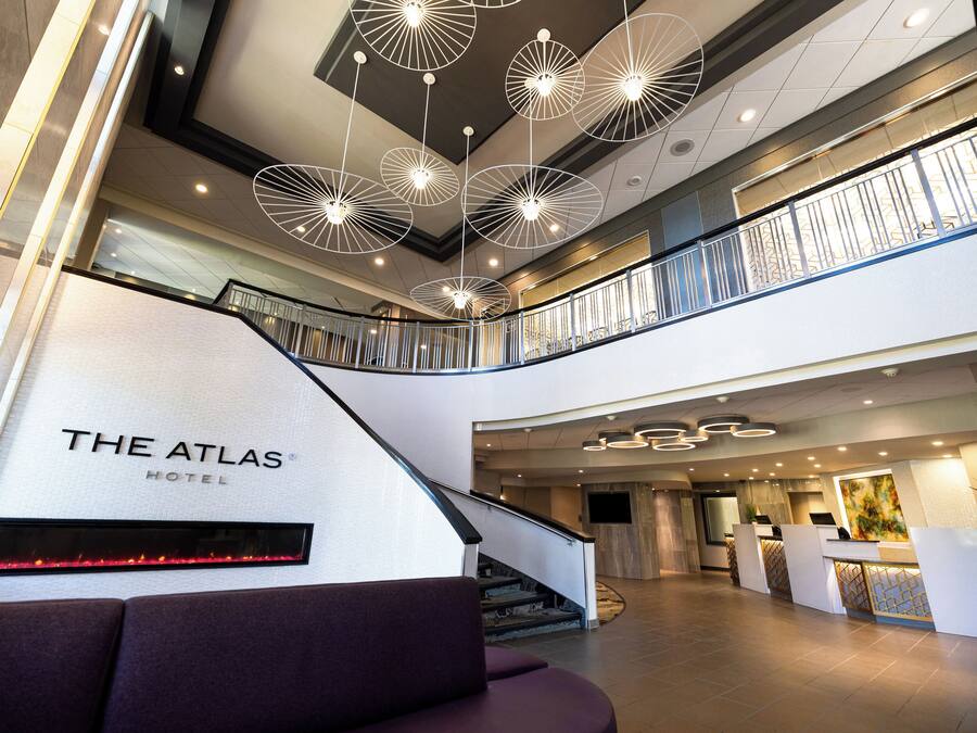 Un vestíbulo de hotel con diseño moderno, que incluye una escalera, mostrador de recepción y un cartel grande que dice 'THE ATLAS HOTEL'.