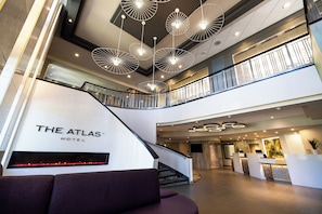 Un vestíbulo de hotel con diseño moderno, que incluye una escalera, mostrador de recepción y un cartel grande que dice 'THE ATLAS HOTEL'.