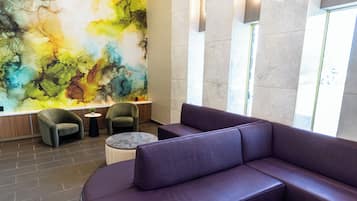 A modern lobby with a large abstract mural, a curved purple sofa, and a marble coffee table.