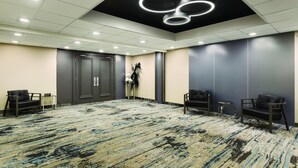 Uma sala de conferências com carpete estampado, paredes escuras e luminárias circulares no teto.