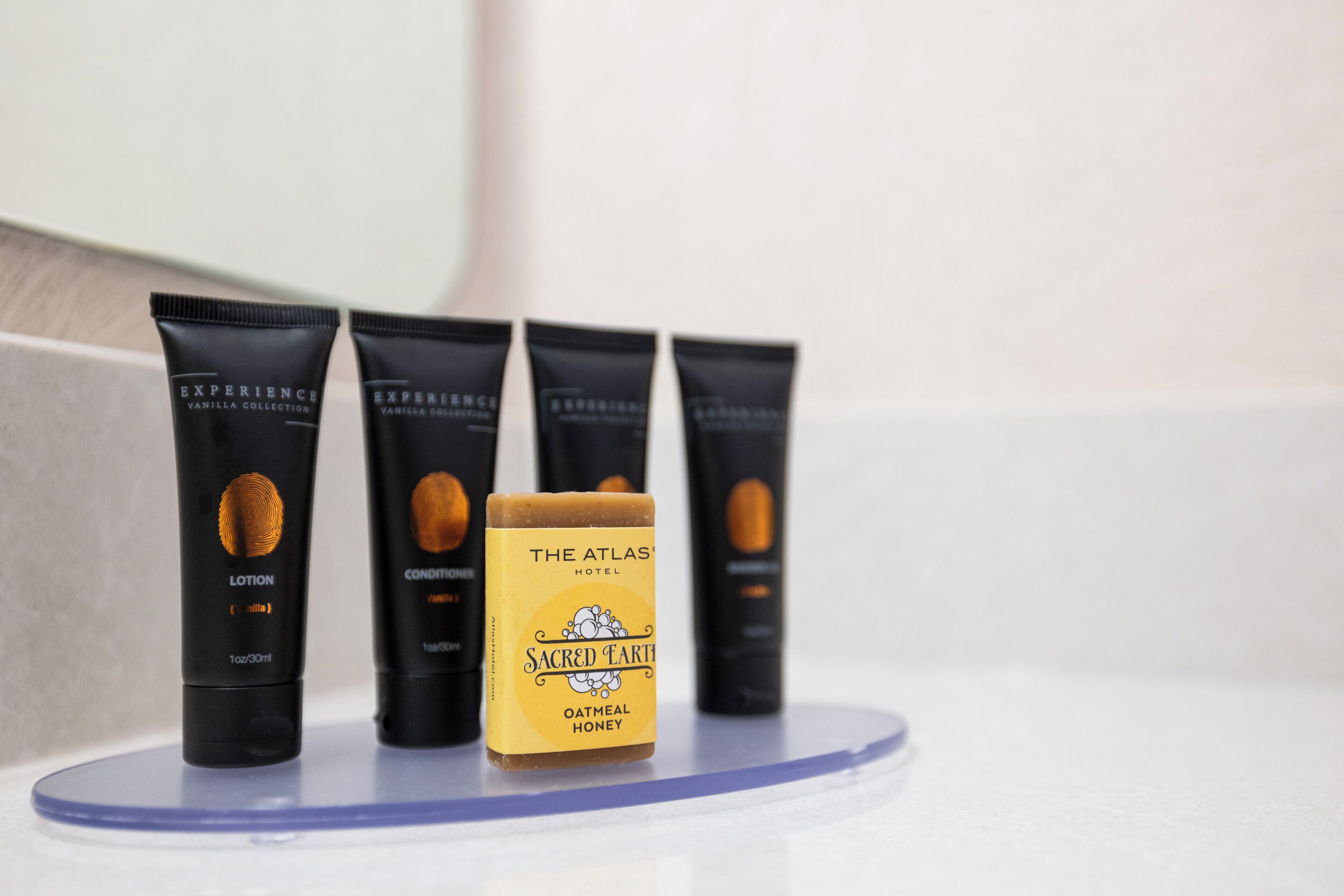 Quatre tubes noirs avec des étiquettes sur une surface blanche, un tube jaune avec une étiquette représentant du miel, et un miroir en arrière-plan.