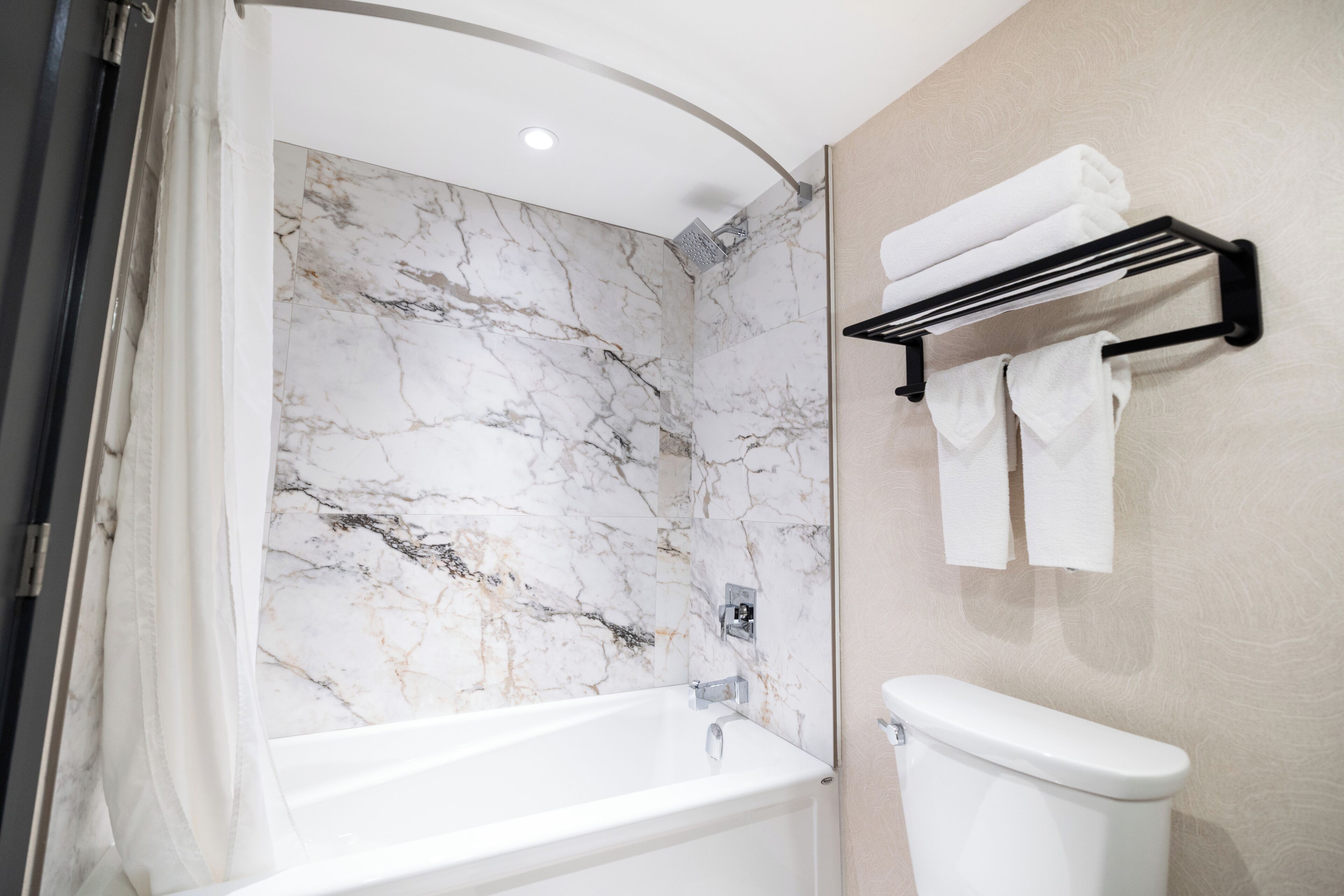 A bathroom with a bathtub, a toilet, and a shower area with a marble wall.