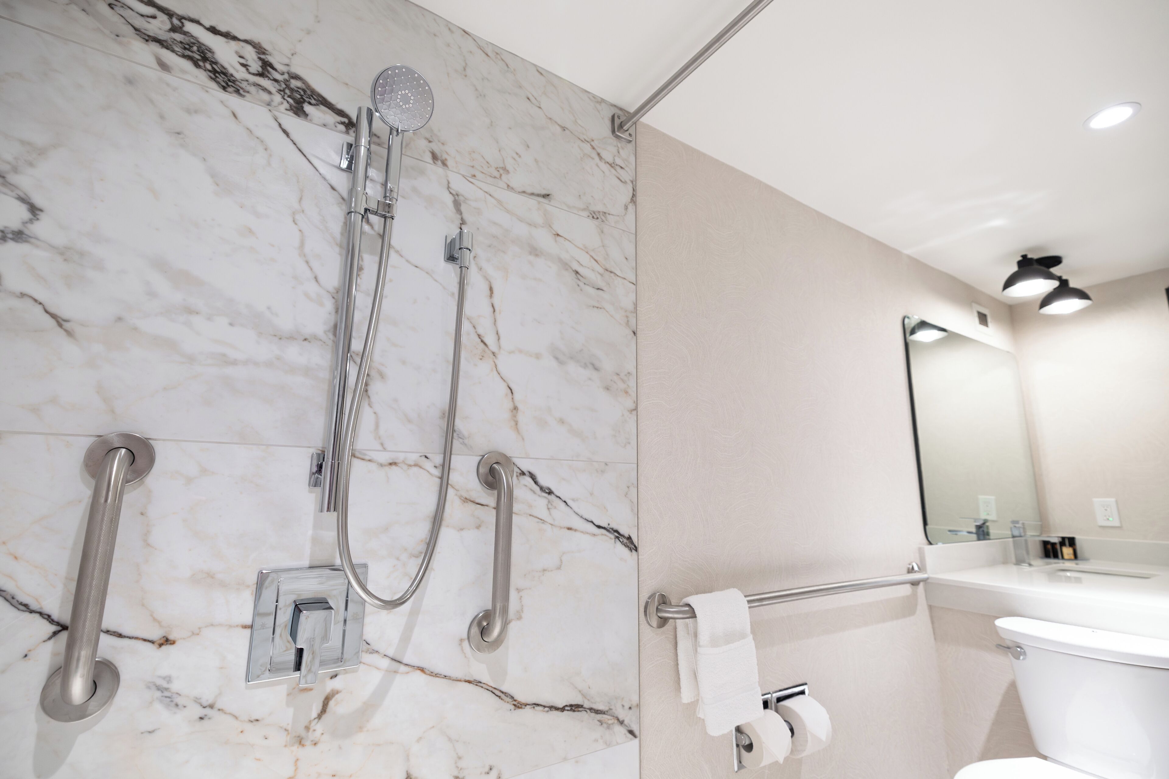 A bathroom with a marble wall, a shower with a handheld showerhead, a towel rack, and a toilet.
