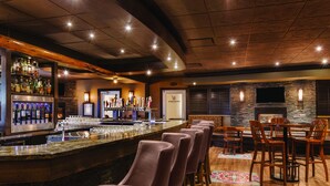 Uma área de bar com um balcão comprido, vários banquetes e uma tela de televisão na parede.