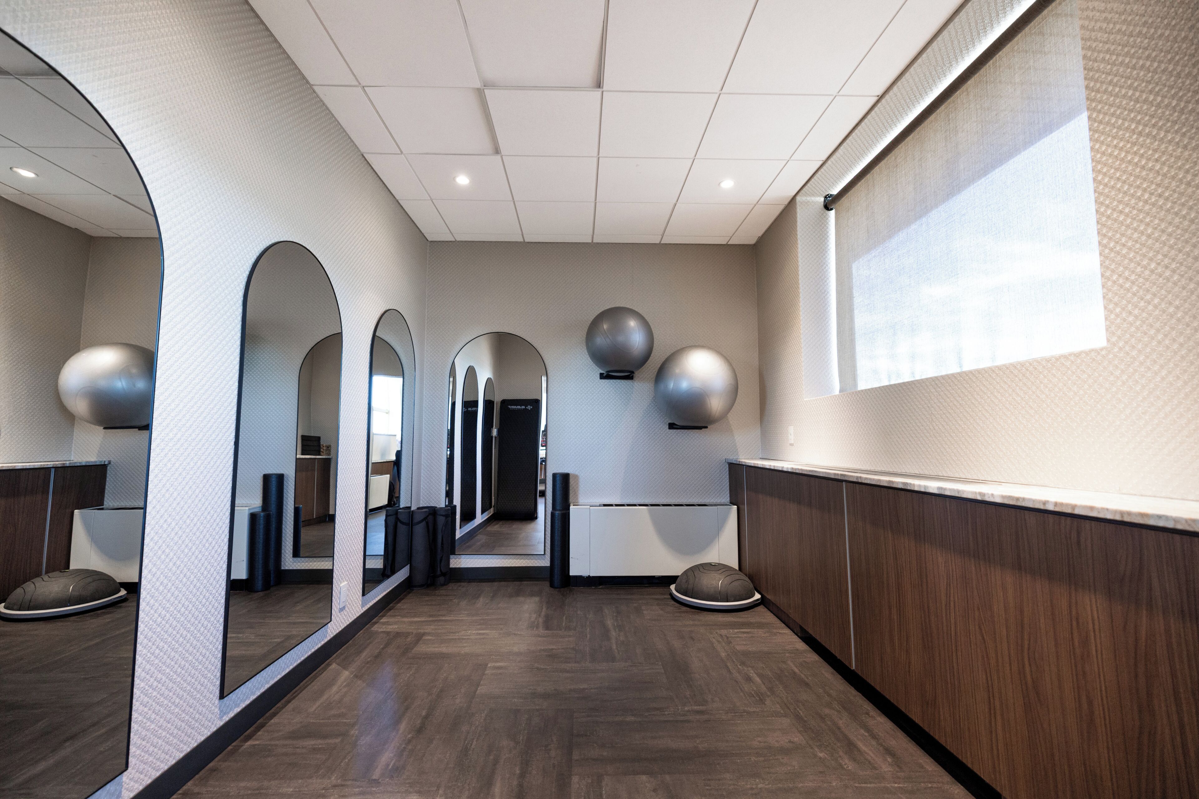 A hallway with mirrored walls, a wooden floor, and exercise balls mounted on the wall.
