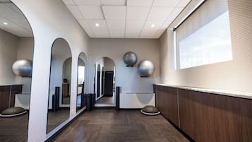 A hallway with mirrored walls, a wooden floor, and exercise balls mounted on the wall.