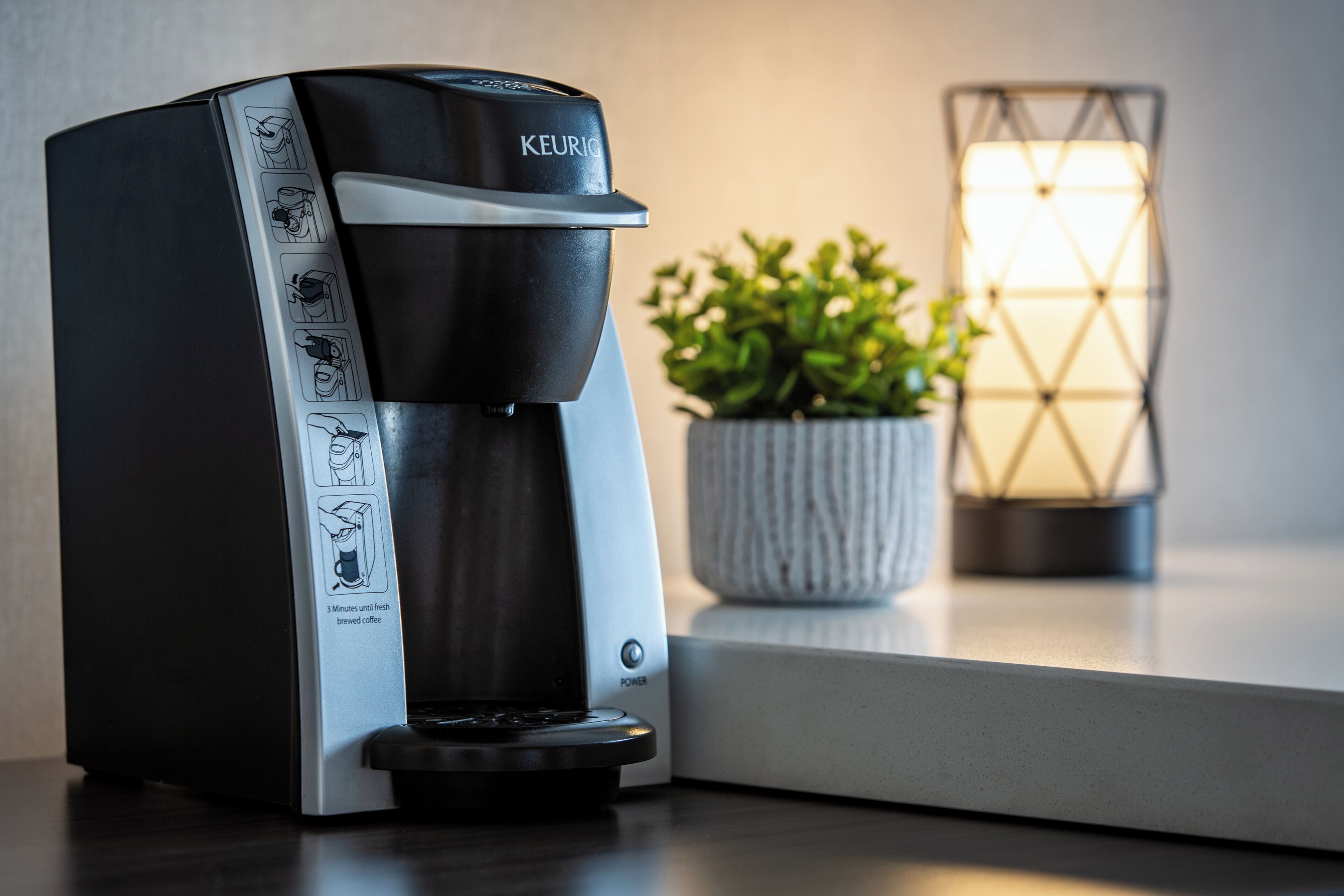 Una cafetera Keurig sobre una encimera con una planta y una vela al fondo.
