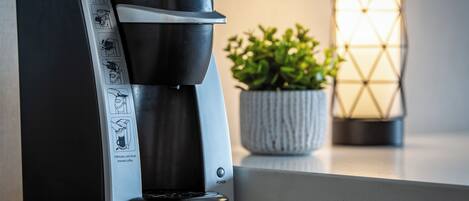 A Keurig coffee maker on a countertop with a plant and a candle in the background.