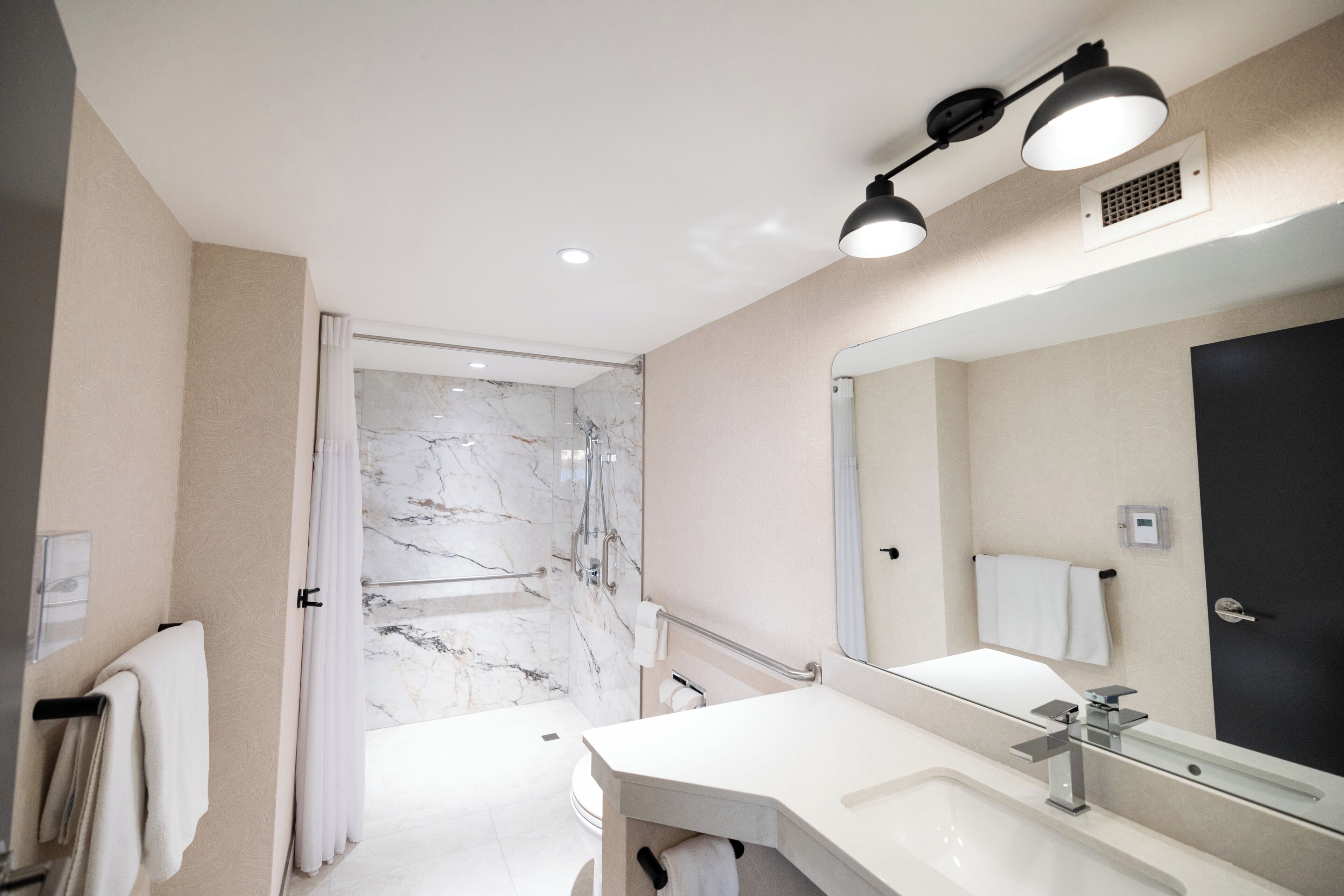 Un baño moderno con ducha de mármol, un espejo grande y un lavabo blanco.