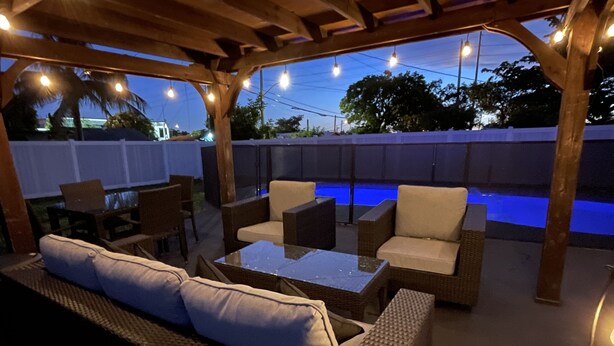 An outdoor patio area with a pool, wicker furniture, and string lights. - MASSIVE HOME WITH HEATED POOL, NEAR BEACH IN SUNNY SOUTH FLORIDA  (Dania Beach)