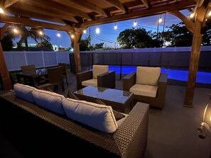 An outdoor patio area with a pool, wicker furniture, and string lights.