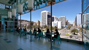 An indoor seating area with tables and chairs, large windows offering a view of the cityscape. - Reina Bilquis (Quito)