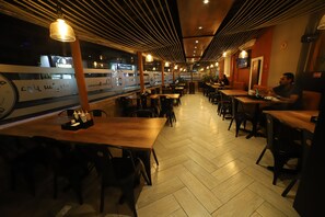 A restaurant with wooden tables and chairs, a tiled floor, and hanging lights. - Reina Bilquis (Quito)