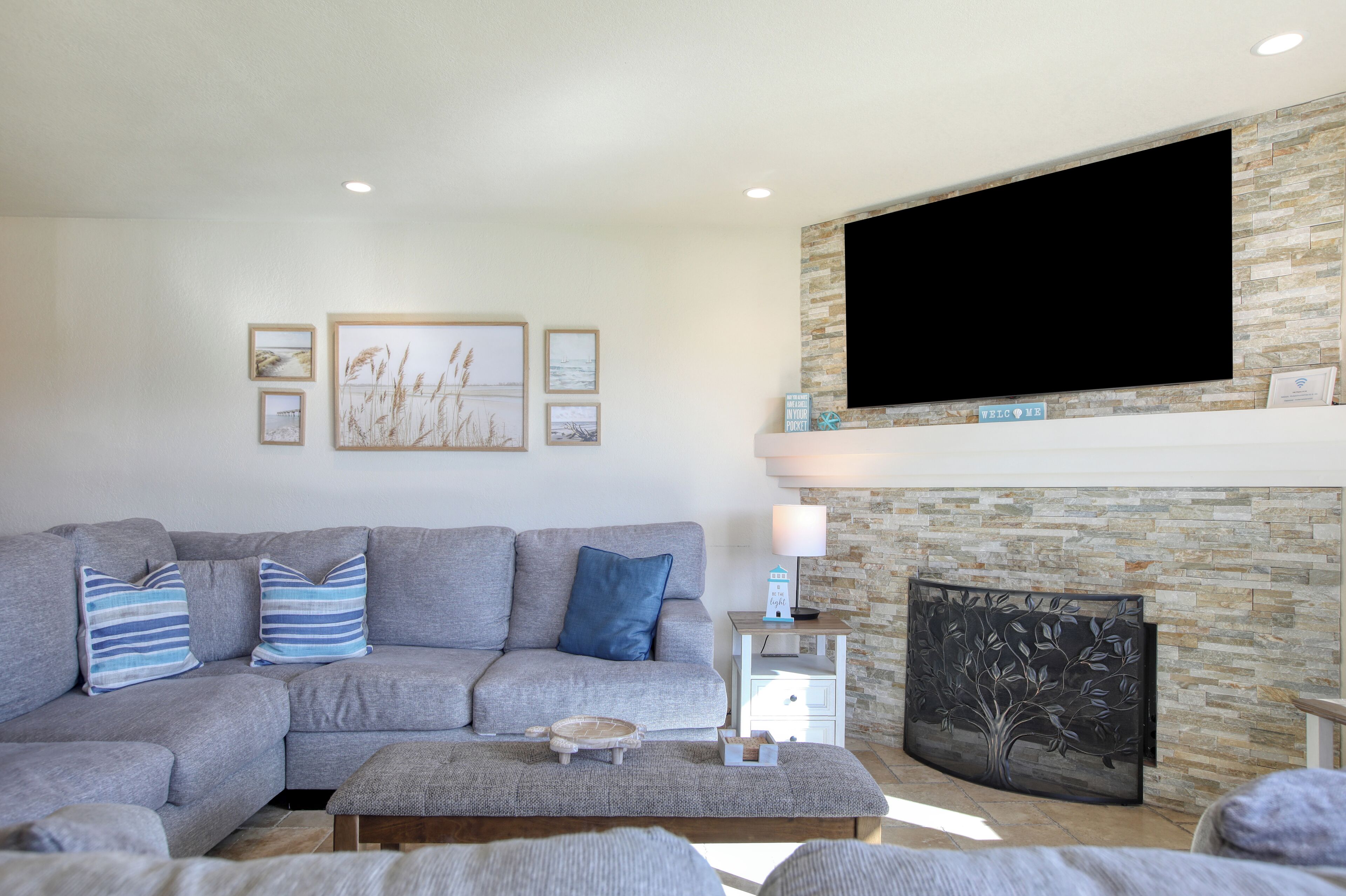 A modern living room with a grey sectional sofa, a coffee table, and a fireplace with a stone accent wall.