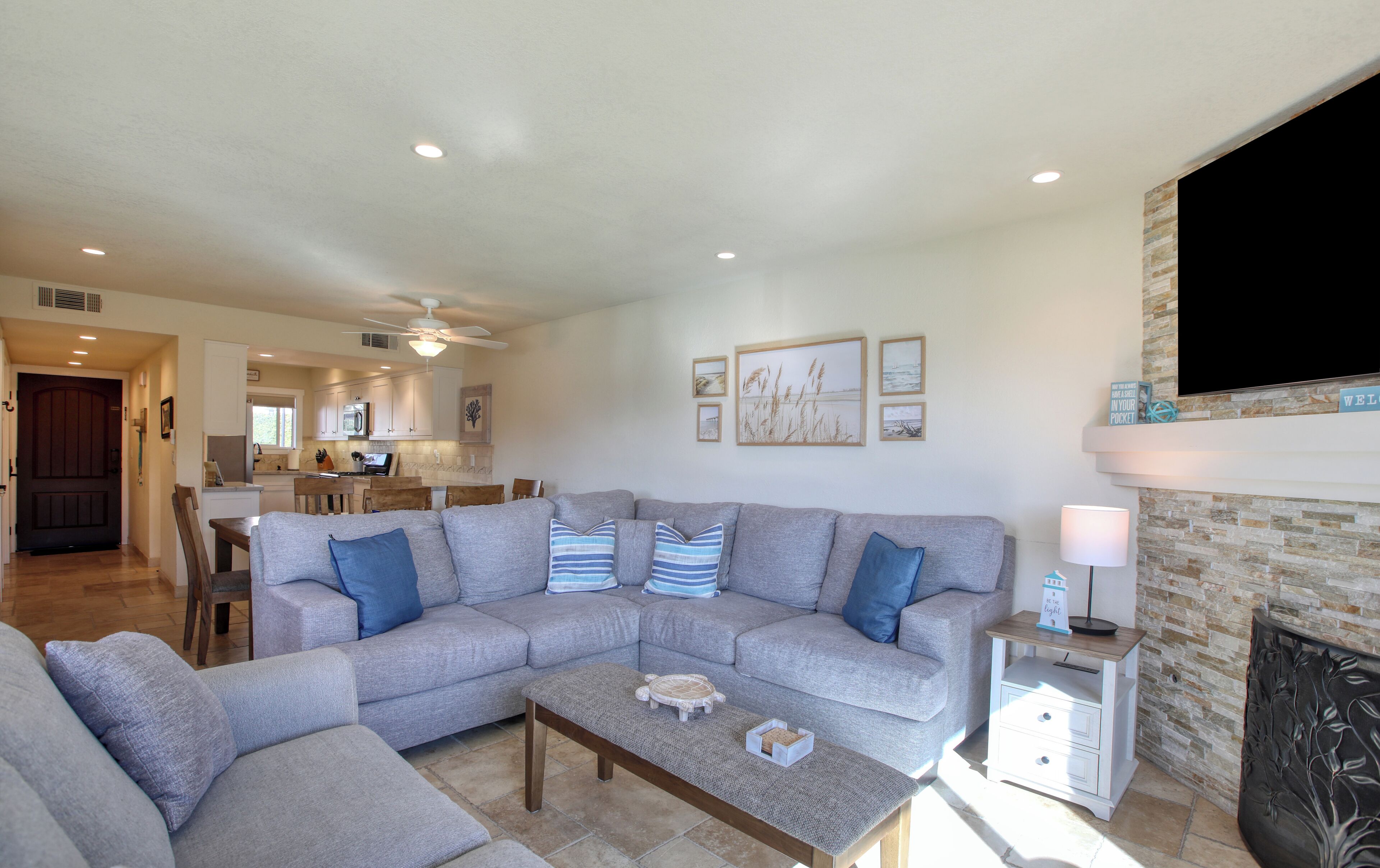 A living room with a sectional sofa, a coffee table, and a TV mounted on a stone wall.
