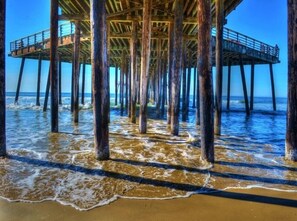 A pier extending into the ocean with wooden supports and a metal railing.
