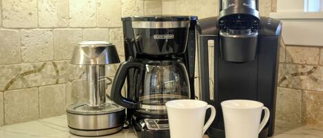 A kitchen with a coffee maker, a kettle, and two white mugs on a marble countertop.