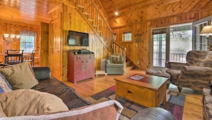 Ein Holzblockhaus-Interieur mit Treppe, Fernseher, Essbereich und Wohnzimmer mit Sofa und Sesseln.
