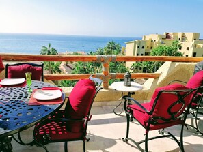 Eine Terrasse mit Tisch und Stühlen, mit Blick auf die Küste, Palmen und Gebäude.